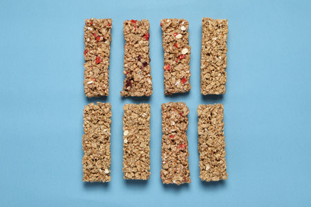 Different tasty granola bars on light blue background, flat lay