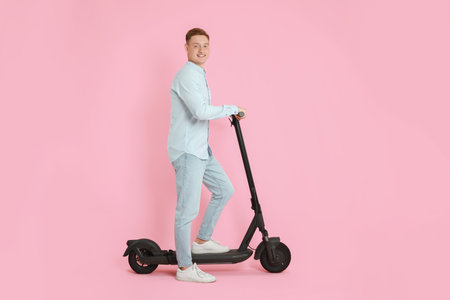 Happy man with modern electric kick scooter on pink backgroundの写真素材