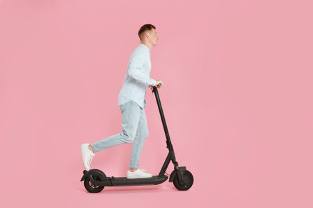 Young man riding modern electric kick scooter on pink backgroundの写真素材