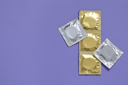 Condom packages on violet background, flat lay and space for text. Safe sexの写真素材
