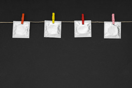 Clothesline with packaged condoms on black background, space for text. Safe sexの写真素材