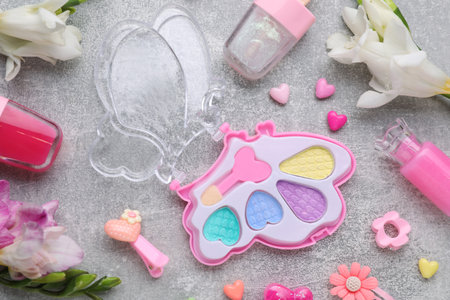 Decorative cosmetics for kids. Eye shadow palette, lipsticks, accessories and flowers on gray table, flat layの写真素材