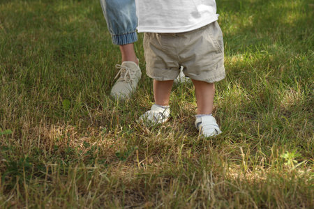 Mother supporting daughter while she learns to walk outdoors, closeup. Space for textの写真素材