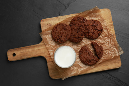 Board with tasty chocolate cookies and glass of milk on dark table, top viewの写真素材
