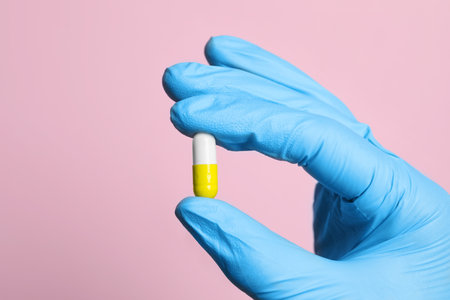 Doctor holding pill on pink background, closeup. Space for textの写真素材