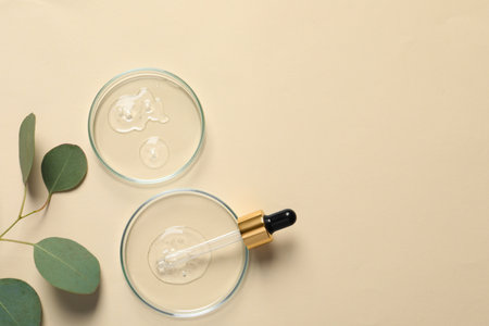 Petri dishes with samples of cosmetic oil, pipette and eucalyptus leaves on beige background, flat lay. Space for textの写真素材