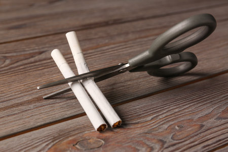 Scissors cutting cigarettes on wooden table. No smoking conceptの写真素材