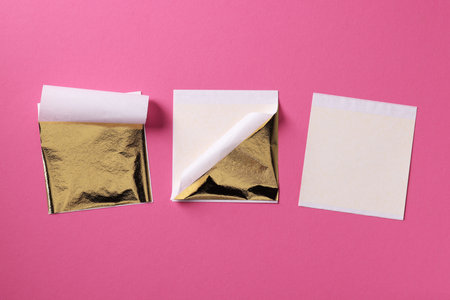 Edible gold leaf sheets on pink background, flat layの写真素材