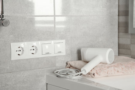 Power sockets, light switches on wall near table with hairdryer and towel indoorsの写真素材