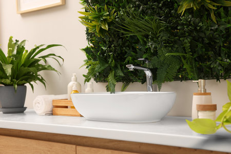 Green artificial plants, vessel sink and various personal care products in bathroomの写真素材