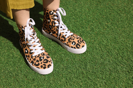Woman wearing sneakers with leopard print on green grass outdoors, closeup. Space for textの写真素材