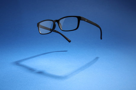 Stylish pair of glasses with black frame on blue background, space for text