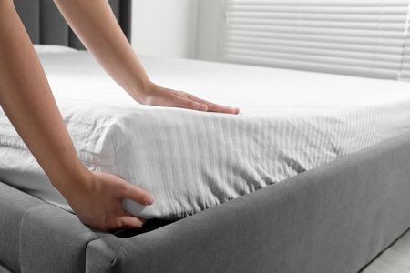 Woman touching soft mattress indoors, closeup view