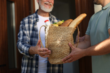 Man with bag of products helping his senior neighbour outdoors, closeupの写真素材