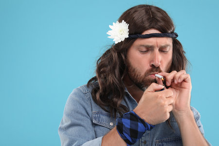Stylish hippie man lighting cigarette on light blue background, space for textの写真素材