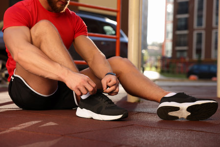 Man tying shoelaces before training at outdoor gym on sunny day, closeup