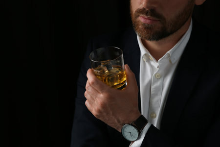 Man holding glass of whiskey with ice cubes on black background, closeupの写真素材
