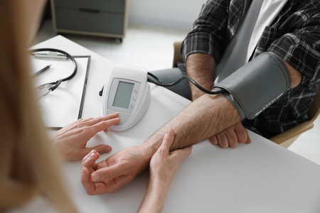 Doctor measuring blood pressure of man at table indoors, closeupの写真素材