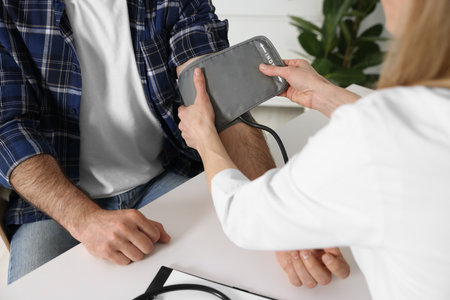 Doctor measuring blood pressure of man at table indoors, closeupの写真素材