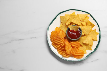 Plate with tasty ketchup, ridged and tortilla chips on marble table, top view. Space for textの写真素材