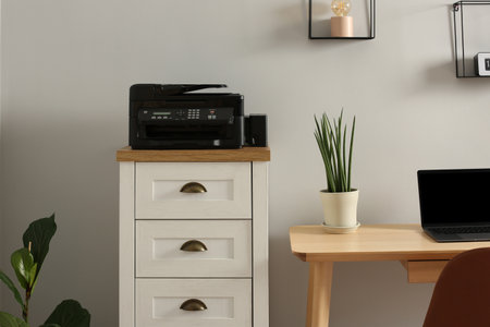 Modern printer on chest of drawers near wooden table indoorsの写真素材