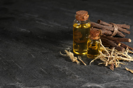 Dried sticks of licorice root and bottles with essential oil on black textured table. Space for textの写真素材