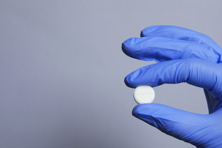 Doctor holding pill on gray background, closeup. Space for textの写真素材