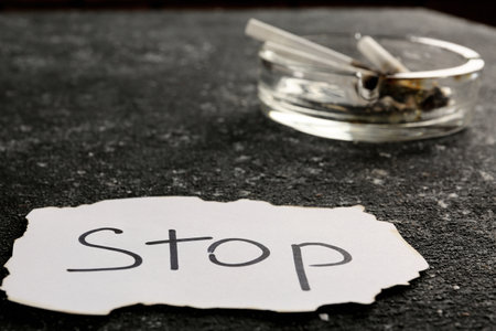Ashtray with burnt cigarettes and the word Stop written on paper on black textured table, closeup. No smoking conceptの写真素材