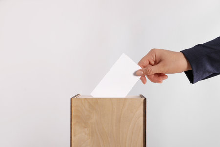 Woman putting her vote into ballot box on light gray background, closeupの写真素材