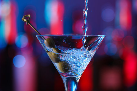 Pouring cocktail into martini glass with olives on blurred background, closeupの写真素材