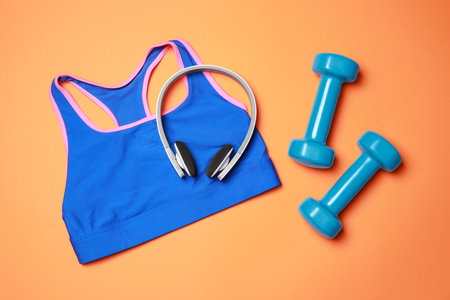 Stylish sports bra, dumbbells and headphones on orange background, flat layの写真素材
