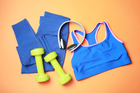 Stylish sportswear, dumbbells and headphones on orange background, flat layの写真素材