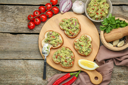 Slices of bread with tasty guacamole and ingredients on wooden table, flat lay. Space for textの写真素材