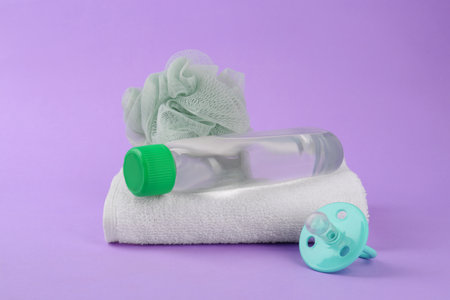 Bottle with baby oil, towel, pacifier and shower puff on violet backgroundの写真素材