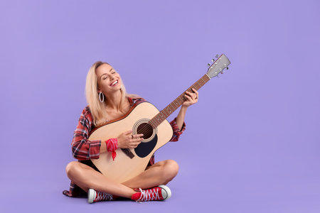 Happy hippie woman playing guitar on purple background. Space for textの写真素材