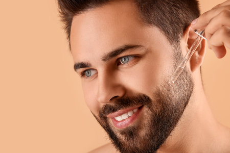 Handsome man applying cosmetic serum onto face on beige background, closeupの写真素材