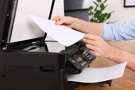 Man using modern printer at wooden table indoors, closeup