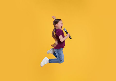 Cute little girl with microphone singing on yellow background