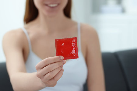 Woman holding condom indoors, closeup. Safe sexの写真素材