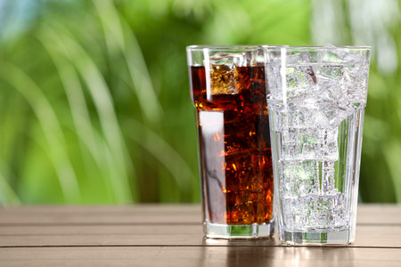 Glasses of different refreshing soda water with ice cubes on wooden table outdoors, space for textの写真素材