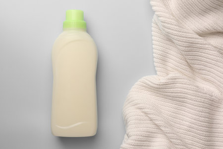 Bottle of fabric softener and white knitted cloth on light background, flat lay. Space for textの写真素材