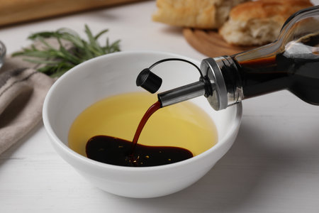 Pouring balsamic vinegar into bowl with oil on white table, closeupの写真素材