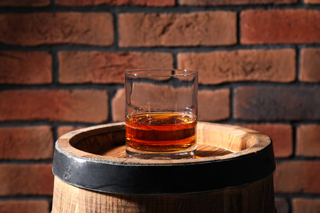 Glass of whiskey on wooden barrel against brick wallの写真素材