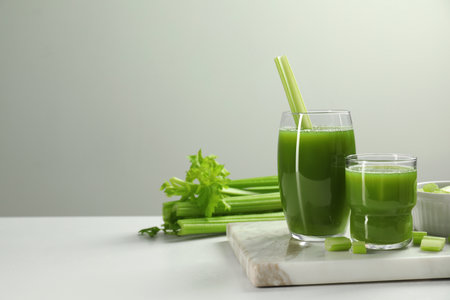 Glasses of delicious celery juice and vegetables on white table. Space for textの写真素材