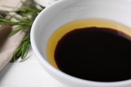 Bowl of balsamic vinegar with oil on white table, closeup