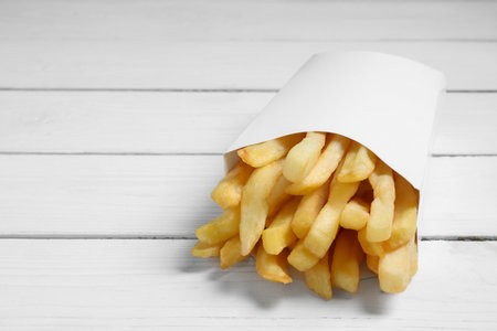Delicious French fries in paper box on white wooden table, closeup. Space for textの写真素材