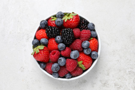 Many different fresh ripe berries in bowl on light gray table, top viewの写真素材