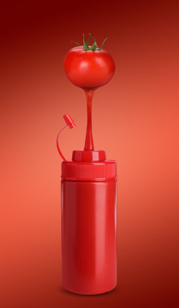 Ketchup made of organic tomatoes. Juice pouring from vegetables into plastic squeeze bottle against red backgroundの写真素材