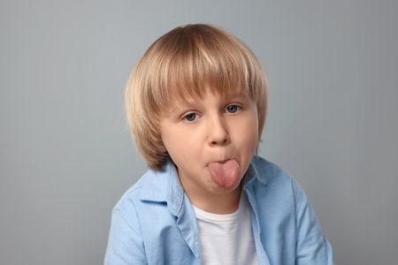 Cute little boy showing his tongue on gray background