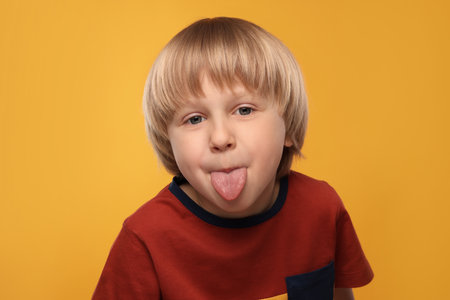 Cute boy showing his tongue on orange backgroundの写真素材